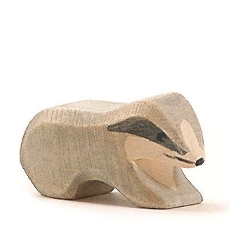 A small handcrafted Ostheimer Badger - Small depicted in a crouching position, artistically carved with visible wood grain and painted features on a plain white background.