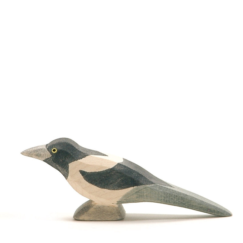 A handcrafted wooden figurine of a Ostheimer Magpie Bird, painted in muted tones with grey, white, and black patches, designed with a simplistic, stylized appearance.