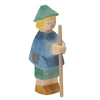 The Ostheimer Shepherd Boy is a handcrafted wooden figurine, likely representing a shepherd. The figure is painted in blue and green with a square hat, blond hair, and carries a wooden staff. Made from sustainably sourced materials, this piece features simple facial details with red lips and blue eyes.