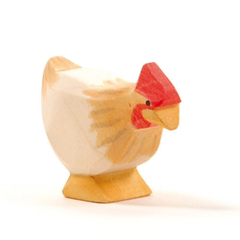 A small wooden figurine of a Ostheimer Hen Standing - Ochre, handcrafted with simple details like red on the comb and hints of brown on the wings, standing upright against a plain white background.