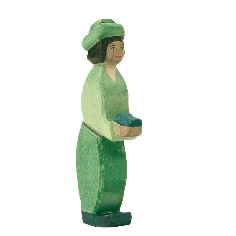 A handcrafted Ostheimer Green King figurine of a woman painted green, wearing a hat and a dress, holding a small black object in her right hand, standing against a plain background.