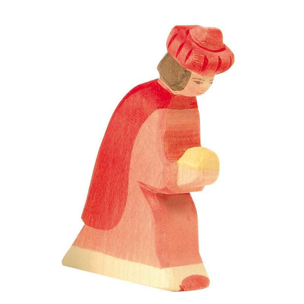 A handcrafted wooden figurine painted in shades of red and beige depicts a person with short dark hair, wearing a red hat and robe. The figure appears to be holding a round object with both hands and is slightly bent forward, sparking imaginative play reminiscent of the Ostheimer Red King.