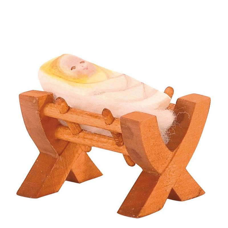 A small handcrafted Ostheimer Baby In Crib figurine of a newborn baby swaddled in a white blanket, resting in a simple, rustic wooden cradle. The baby and cradle are carved with minimalist details.