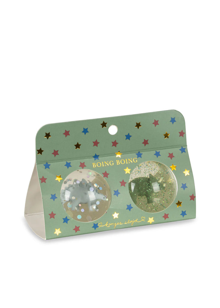 The Konges Sloejd Glitter Bouncing Ball Set - Dinosaurs features two glittery bouncing balls in a green, star-patterned "BOING BOING" package with clear windows, gold accents, and playful text at the bottom.
