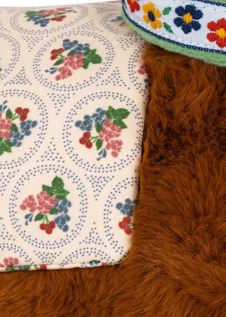 Close-up of a Konges Sloejd Fiona Horse cuddly toy with brown fur, a floral patterned saddle, and a green harness with embroidered flowers.