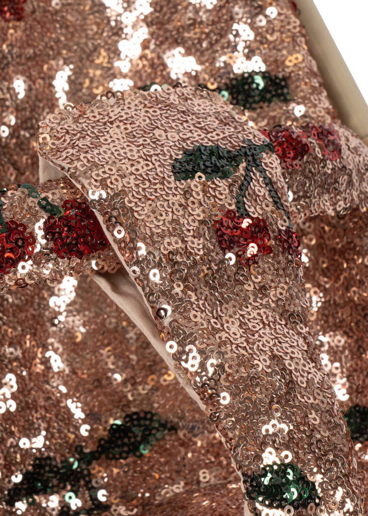 Close-up of the Konges Sloejd Sparkly Doll Stroller - Cherry Sequin fabric covered in shimmering gold sequins and a repeating cherry pattern with red fruit and green leaves.