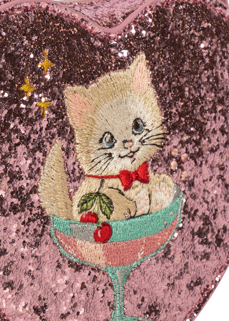 Konges Sloejd Tut Kitty Shoulder Bag is a heart-shaped pink sequined bag featuring an embroidered kitten wearing a red bow tie, sitting inside a glass with cherries.