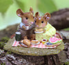 The Wee Forest Folk Tiny Collectible – Just the Two of Us (Not a Toy) features two hand-sculpted mice on a log picnic, sharing sandwiches, watermelon, a thermos, and fruit—one in a shirt, the other in a yellow dress. Detailed and whimsical.