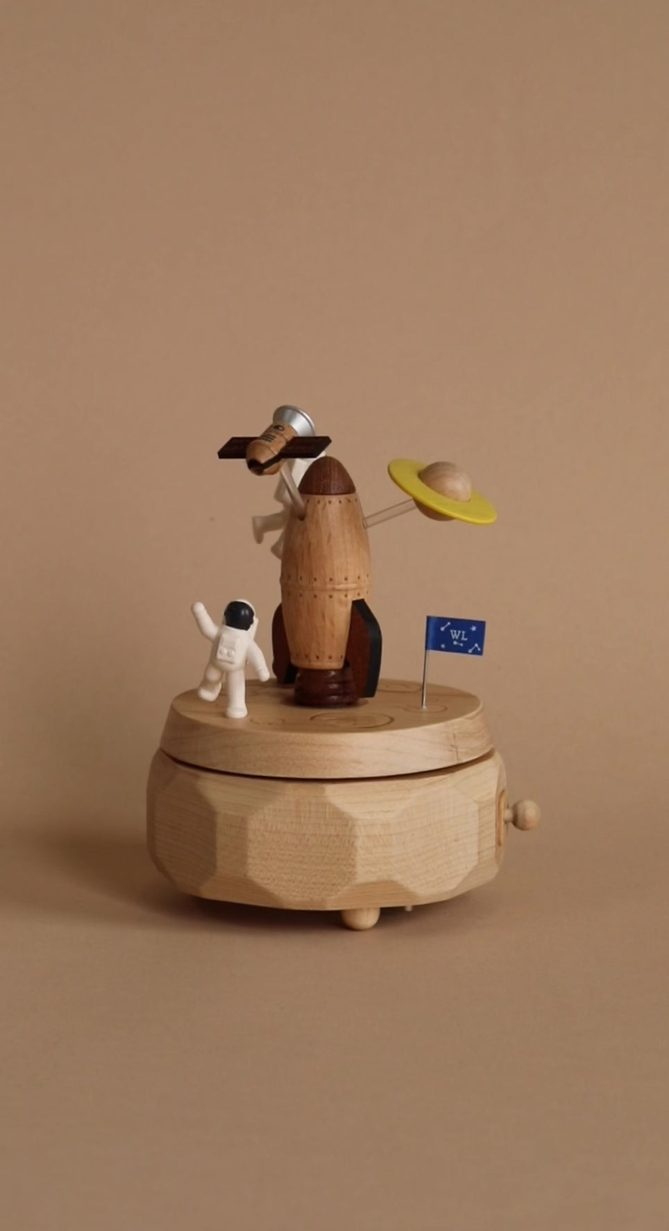 Space themed wooden music box with a rocket in the middle and astronauts and spaceships going around it. 