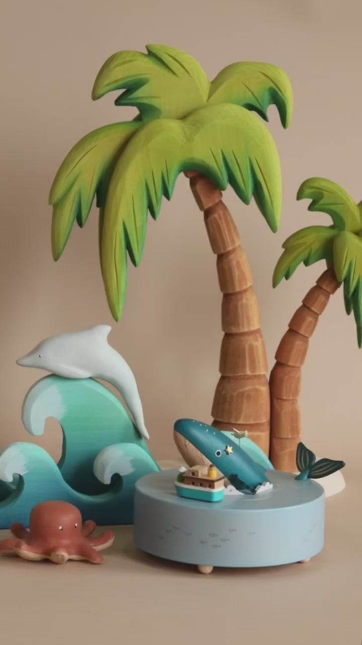 Wooden ocean themed music box with a blue whale in the center and a boat going around it. Palm trees and waves in the background. 