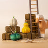 Three wooden pumpkins in green, yellow, and white sit on brown blocks by a toy horse and ladder—a charming Bumbu Handmade Wooden Pumpkin Patch Set for Montessori play in a neutral setting.