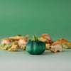 A small green pumpkin sits on a light surface with dry leaves and wooden hedgehog figurines from the Bumbu Handmade Wooden Pumpkin Patch Set. A soft green gradient background makes it ideal for Montessori play.