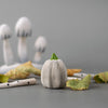A small gray pumpkin with a green stem sits among yellow leaves and white objects with black markings—perfect for Montessori play or adding to your Bumbu Handmade Wooden Pumpkin Patch Set.
