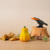 A small yellow gourd among dried leaves and twigs, with a black bird figurine in the background—perfect for Montessori play or paired with the Bumbu Handmade Wooden Pumpkin Patch Set.