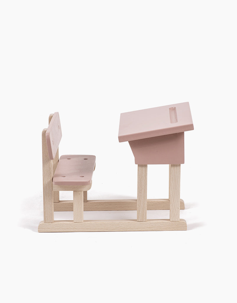 Introducing the Minikane Doll School Desk in Powder Pink: a charming handmade wood model of a traditional school desk and attached bench seat, both painted in a delightful pastel pink. The desk features a slanted surface with a groove for holding writing implements, making it perfect for your Minikane Babies and adding a touch of charm to any setting.