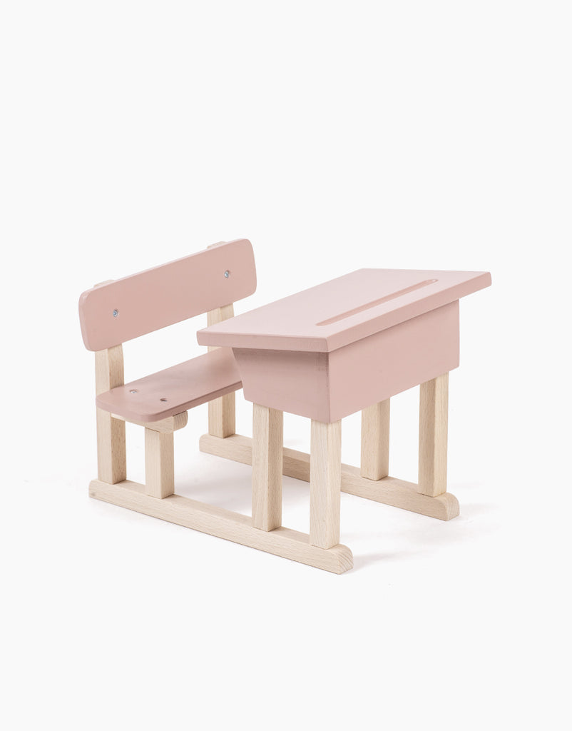 A small, powder pink wooden Minikane Doll School Desk with an attached bench. This set features a minimalistic design with unpainted wooden legs and braces, reminiscent of items crafted for Minikane Babies, and is set against a plain white background.