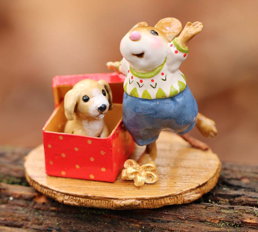 A joyful, hand-sculpted mouse in festive clothes stands by a red box with a tiny dog on a round wooden base. This Wee Forest Folk Tiny Collectible - Christmas Critter (Not a Toy) brings whimsy to any collection.