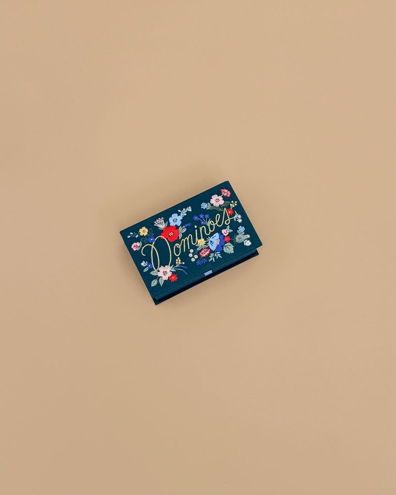 A rectangular dark blue card with colorful floral designs and "Strawberry Fields Dominoes Set" in decorative script, displayed on a plain beige background.