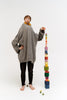 A young boy in an oversized grey sweater and black pants stands barefoot next to Raduga Grez | Big Cube Block Set - Colorful. He appears serious and is pointing at the top block.
