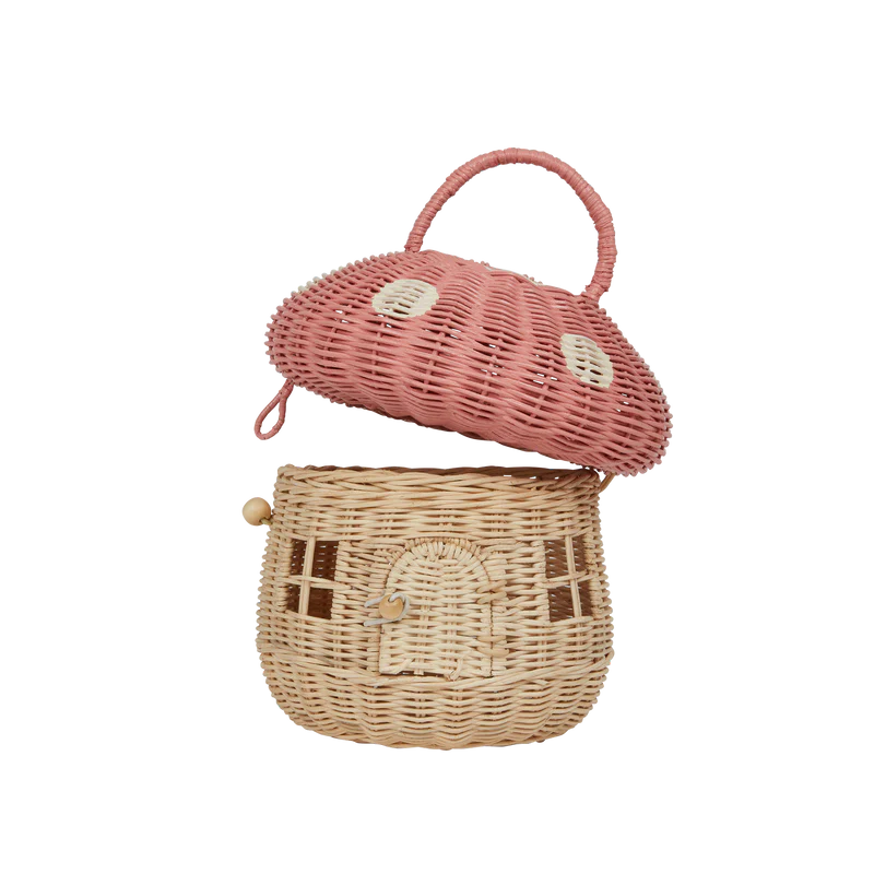 A whimsical handwoven Olli Ella Mushroom Basket in Pink designed to resemble a cottage, featuring a pink roof, windows, and a door, complete with a wooden latch and handle.