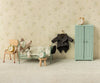 A collectible Maileg Wedding Mice Couple in Box, Mum and Dad, lies in a bed beside a wardrobe, hanging coat, chair, and stool. Four alarm clocks are placed on the furniture within this miniature, vintage-style bedroom—perfect for collectors of Maileg wedding mice or as a charming wedding gift.