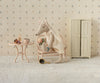 A Maileg Wedding Mice Couple in Box, Mum and Dad, are seated together—she dressed as a bride holding flowers on a bench beside a small table with a cup, mirror, and perfume, with a cream wardrobe against a patterned wall—creating an enchanting scene perfect for collectors or as a whimsical wedding gift.