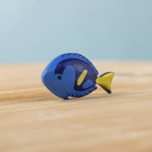 The Bumbu Handmade Wooden Royal Blue Fish is a small, sustainably crafted Montessori toy, painted blue with dark blue and yellow details. It stands upright on a wooden surface—a charming choice for imaginative play.