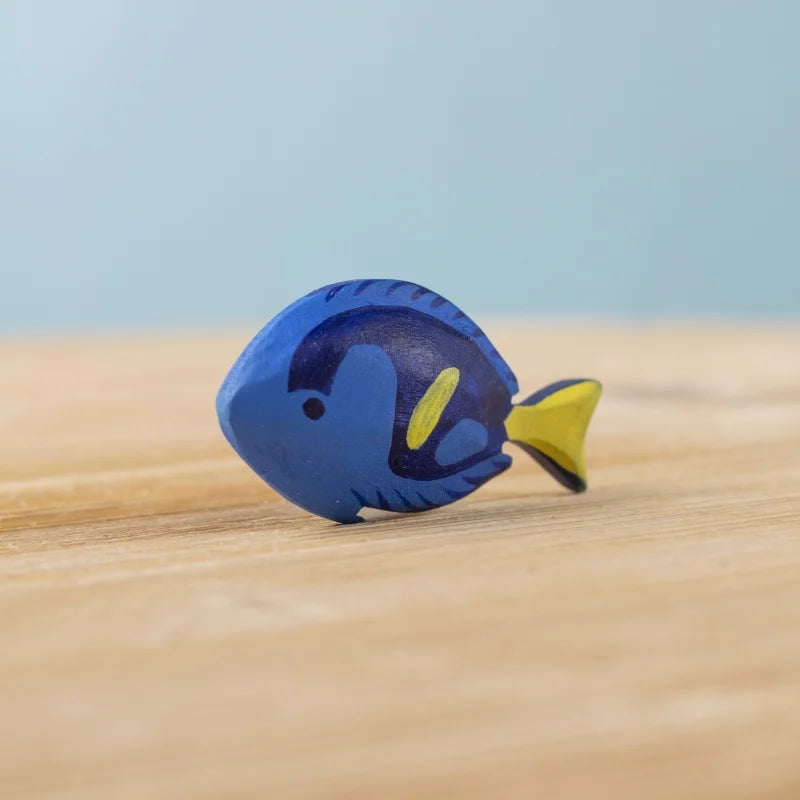 The Bumbu Handmade Wooden Royal Blue Fish is a small, sustainably crafted Montessori toy, painted blue with dark blue and yellow details. It stands upright on a wooden surface—a charming choice for imaginative play.