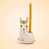A Royal White Rabbit Cake Topper, featuring a handcrafted white ceramic rabbit adorned with a gold crown and carrying a yellow candle on its back, makes a charming accent for any space. Shown here against a plain light beige background.