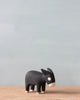A small black Handmade Tiny Wooden Farm Animals - Donkey figurine, with white details on its face and ears, stands on a wooden surface against a plain light blue background.