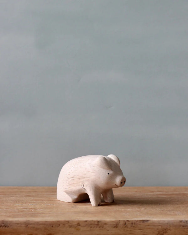A small Handmade Tiny Wooden Farm Animals - Pig figurine on a wooden surface, set against a soft grey background.