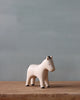 A Handmade Tiny Wooden Farm Animals - Horse figurine on a wooden surface against a soft gray background. The horse is painted white with black features.