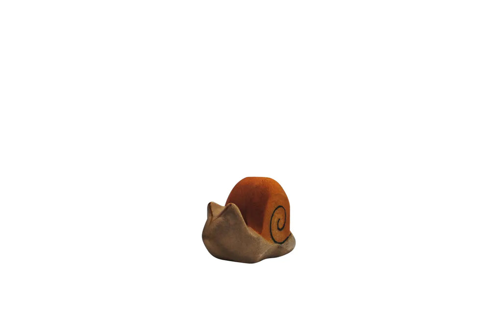The Handmade Holzwald Snail, a small and simple clay sculpture with an orange shell and beige body inspired by Holzwald's sustainable toys, is centered on a white background.