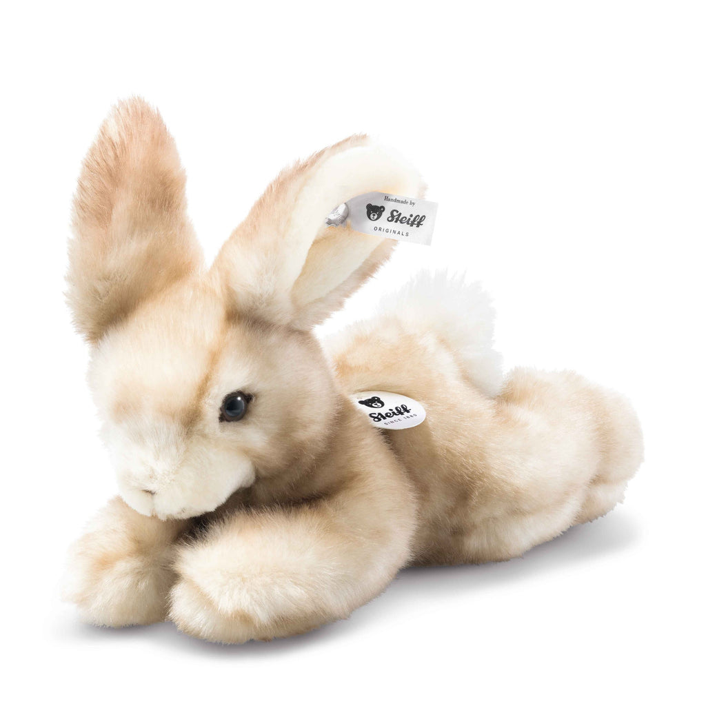 The Steiff Schnucki Rabbit is a light brown plush with white accents, soft fur, upright ears, black eyes, and Steiff tags in its ear and on its side. This hand-crafted collectible is made in Germany.