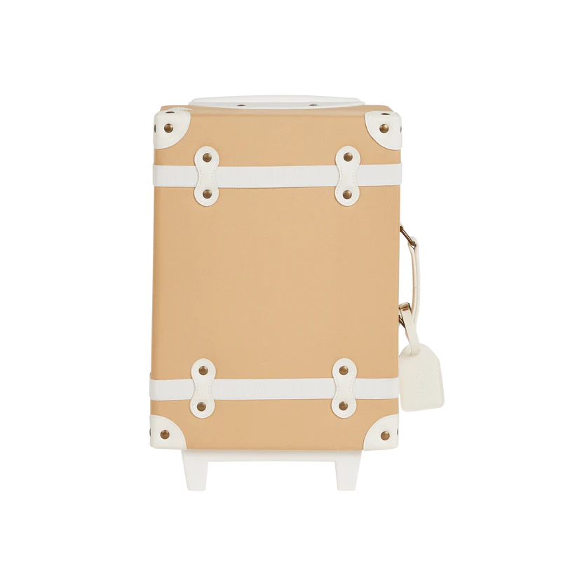 A carry-on sized Olli Ella See-Ya Suitcase - Butterscotch with white straps and metal buckles, viewed from the side against a transparent background.