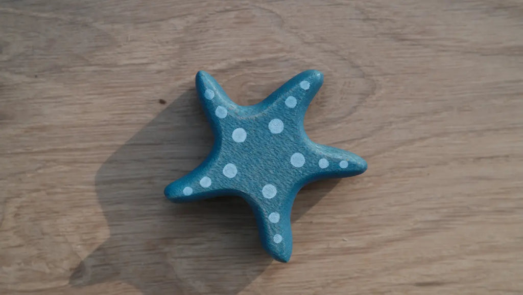 The Handmade Holzwald Starfish, a blue wooden toy with white polka dots, sits on a light wood surface and casts a left shadow—an adorable, sustainable addition to any toy collection.