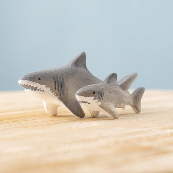 Two Bumbu Handmade Wooden Shark Family Set figurines, one large and one small, are displayed side by side on a light wooden surface against a plain blue background.