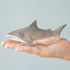 A hand holds a small, gray shark toy from the Bumbu Handmade Wooden Shark Family Set against a light blue background—ideal for Montessori collections or as part of your Shark Family set.