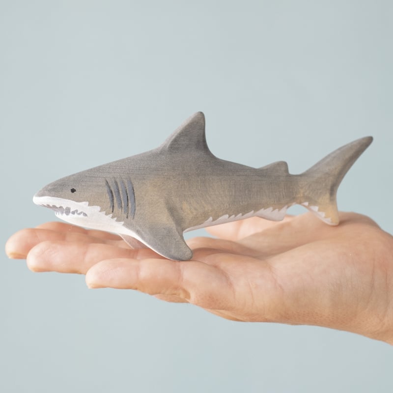 A hand holds a small, gray shark toy from the Bumbu Handmade Wooden Shark Family Set against a light blue background—ideal for Montessori collections or as part of your Shark Family set.