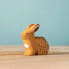 The Bumbu Handmade Wooden Sitting Rabbit is a small, handcrafted light brown toy with white spots and a white heart on its side, shown on a wooden surface against a light blue background.
