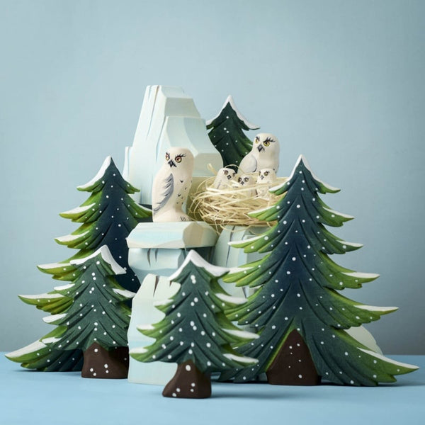 The Bumbu Handmade Wooden Snowy Owl Wilderness Set features pine trees, a snowy mountain, and white owl figurines—an eco-friendly Montessori toy ideal for learning and play against a serene blue backdrop.