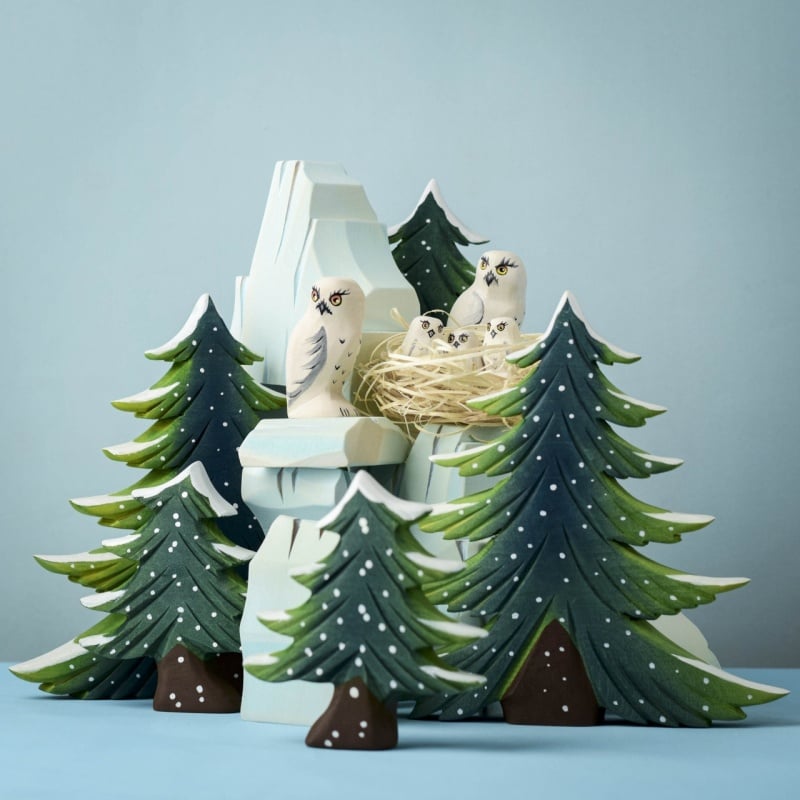 The Bumbu Handmade Wooden Snowy Owl Wilderness Set features pine trees, a snowy mountain, and white owl figurines—an eco-friendly Montessori toy ideal for learning and play against a serene blue backdrop.