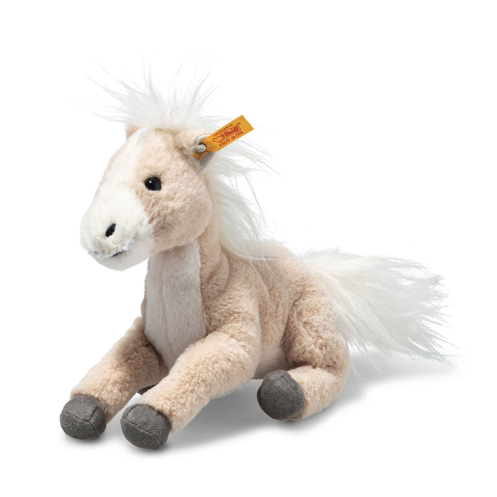 The Steiff Gola Dangling Horse, a soft plush toy with light beige fur, white mane and tail, gray hooves, and a yellow ear tag, sits upright against a white background.
