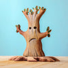 A Bumbu Handmade Wooden Halloween Trees With Hanging Bat toy, featuring a carved tree with hollow eyes, a frowning mouth, and small green leaves on its branches.