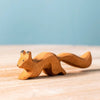 The Bumbu Handmade Wooden Squirrel Running, a small handcrafted beechwood figurine, sits on a light wood surface with a soft blue background, ready to spark imaginative forest adventures.