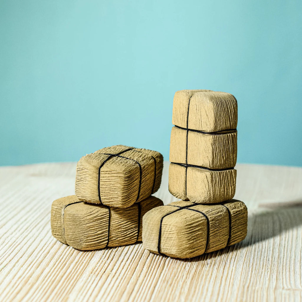 Four stacks from the Bumbu Handmade Wooden Haystacks Set, wrapped in brown paper and tied with black string, resemble mini straw bales—ideal for imaginative play or farm toy displays against a blue background.
