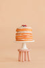 A stack of pancakes topped with berries sits on a white cake stand with a beaded edge, which rests on the Maileg Stool Set, Mouse in Light Rose/Light Mint, set against a beige background.