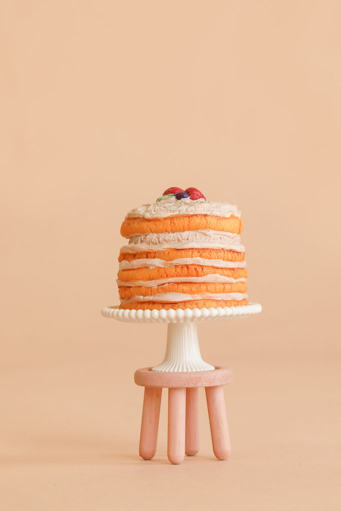 A stack of pancakes topped with berries sits on a white cake stand with a beaded edge, which rests on the Maileg Stool Set, Mouse in Light Rose/Light Mint, set against a beige background.