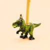 Introducing the T-Rex Cake Topper – Final Sale: This handcrafted porcelain figurine features a small green dinosaur wearing a festive party hat and carrying a yellow candle on its back, accented with delicate touches of gold. Set against a plain beige background, this collectible piece adds a charming flair to any celebration.