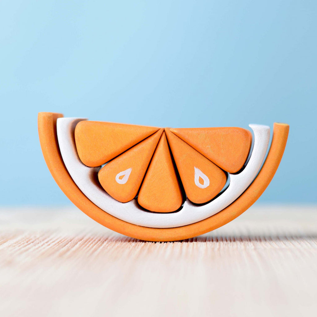 A creatively designed Wooden Tangerine Stacking Toy made from layers of white and orange materials, displayed on a light natural wood surface against a soft blue background.
